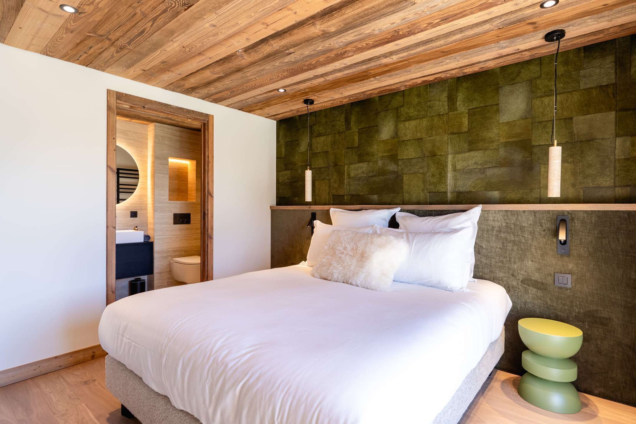 Un dormitorio moderno con techo de madera, una cama grande, una mesita de noche y una lámpara fijada a la pared.