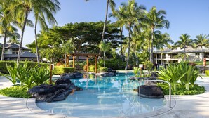 Una piscina de resort con palmeras, un pabellón y un jardín cuidado.