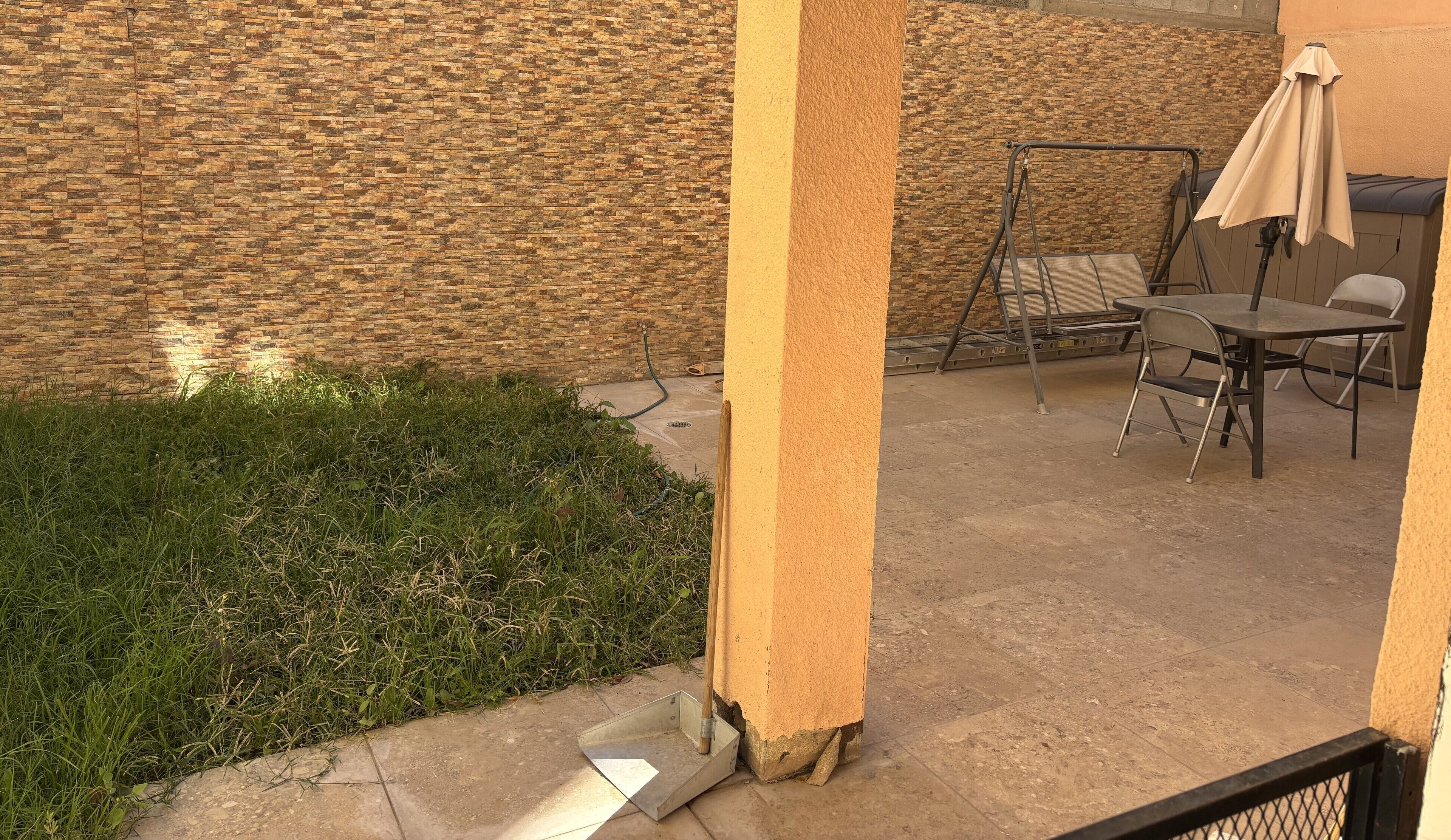 A patio area with a stone wall, a grassy area, and outdoor furniture including a table and chairs.