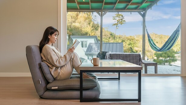A person sitting on a modern chair by a large window with a view of trees and a hammock. - Gangneung Dawon-hill Pension (Gangneung)