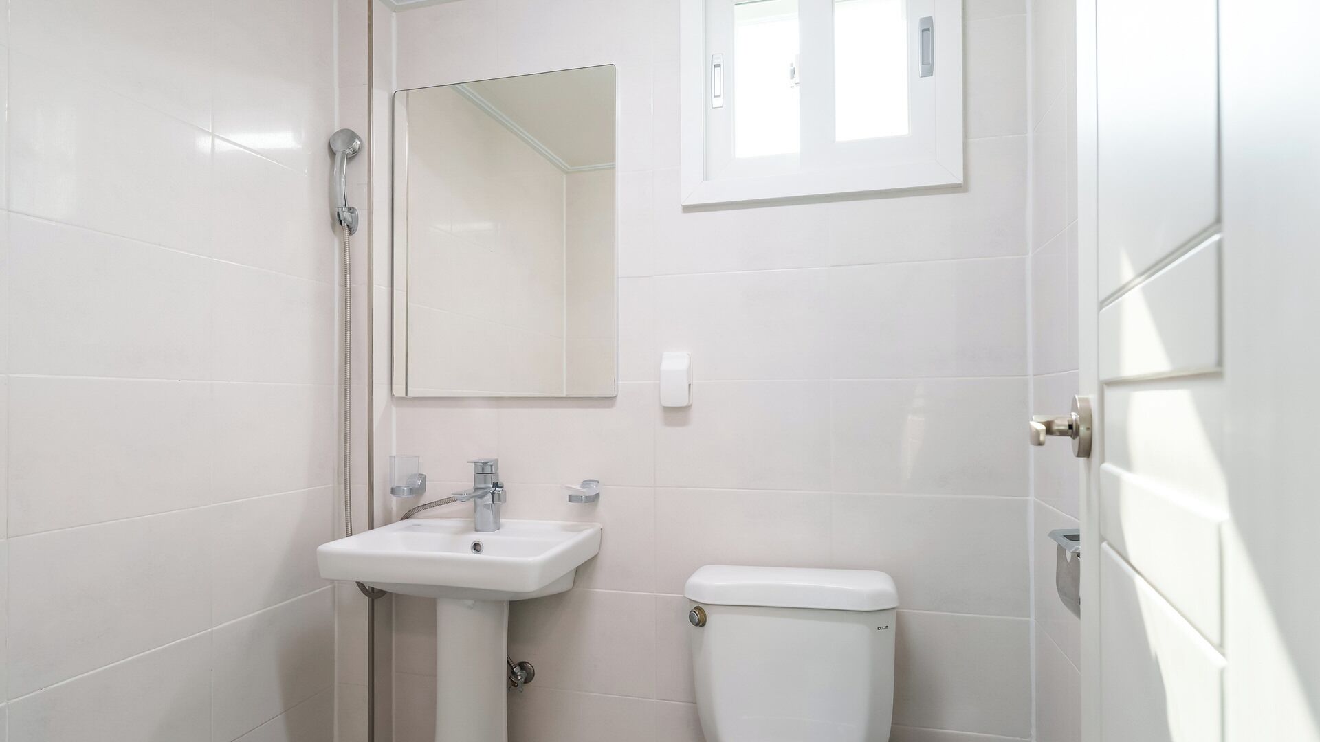 Een badkamer met witte tegels, een wastafel, toilet, spiegel en douche.