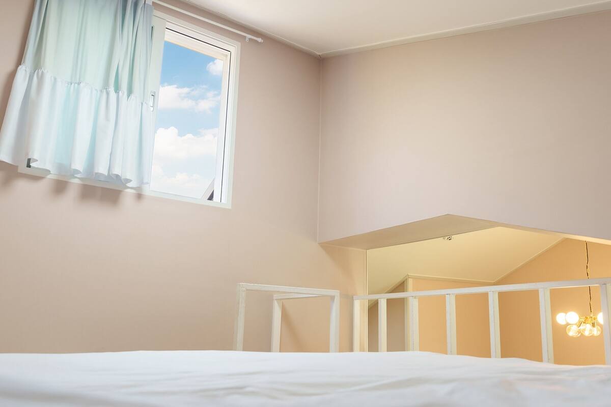 Un dormitori amb un llit, una finestra amb cortines, un mirall i una làmpada.