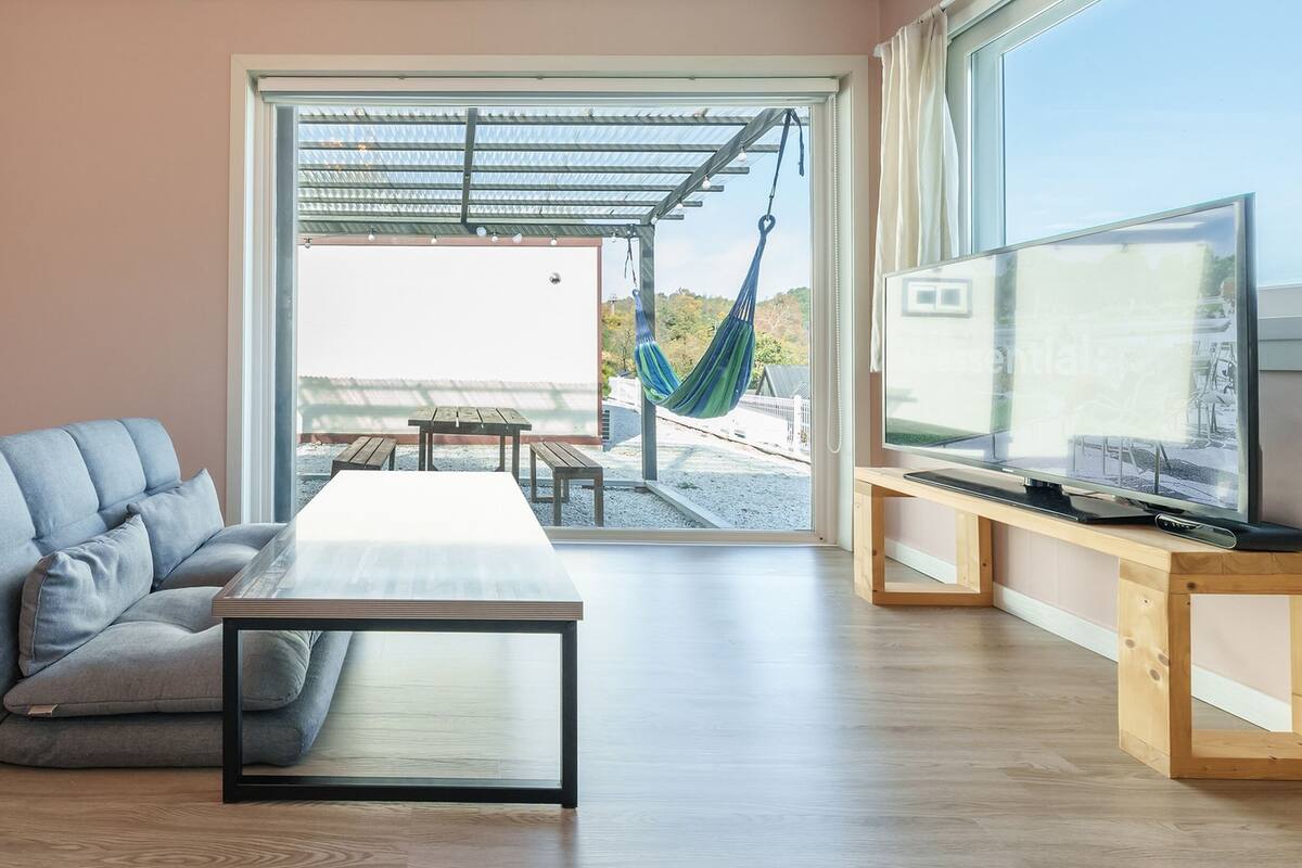 Un saló modern amb un sofà, una taula de centre, una televisió sobre un suport de fusta i una cadira espanyola a la porta.