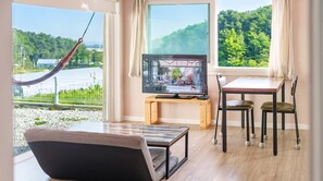 Une chambre moderne équipée d’une télévision, d’une table à manger, de chaises et offrant une vue sur un paysage verdoyant.