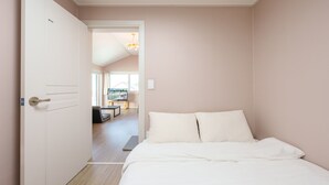 A bedroom with a bed, a door, and a view into another room with a TV and a table. - Gangneung Dawon-hill Pension (Gangneung)