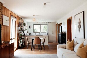 A modern kitchen with a dining area, wooden walls, and a large window.