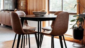 A dining area with a brick wall, wooden paneling, a large window, and a hanging light fixture. - StudioNESS Scamander (Break O'Day)