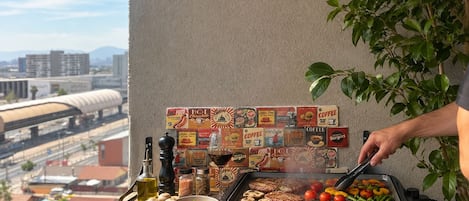 A person grilling food on an outdoor grill with a cityscape view in the background.