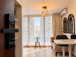Una sala de estar moderna con cerradura digital, una zona de comedor y ventanas amplias con cortinas.