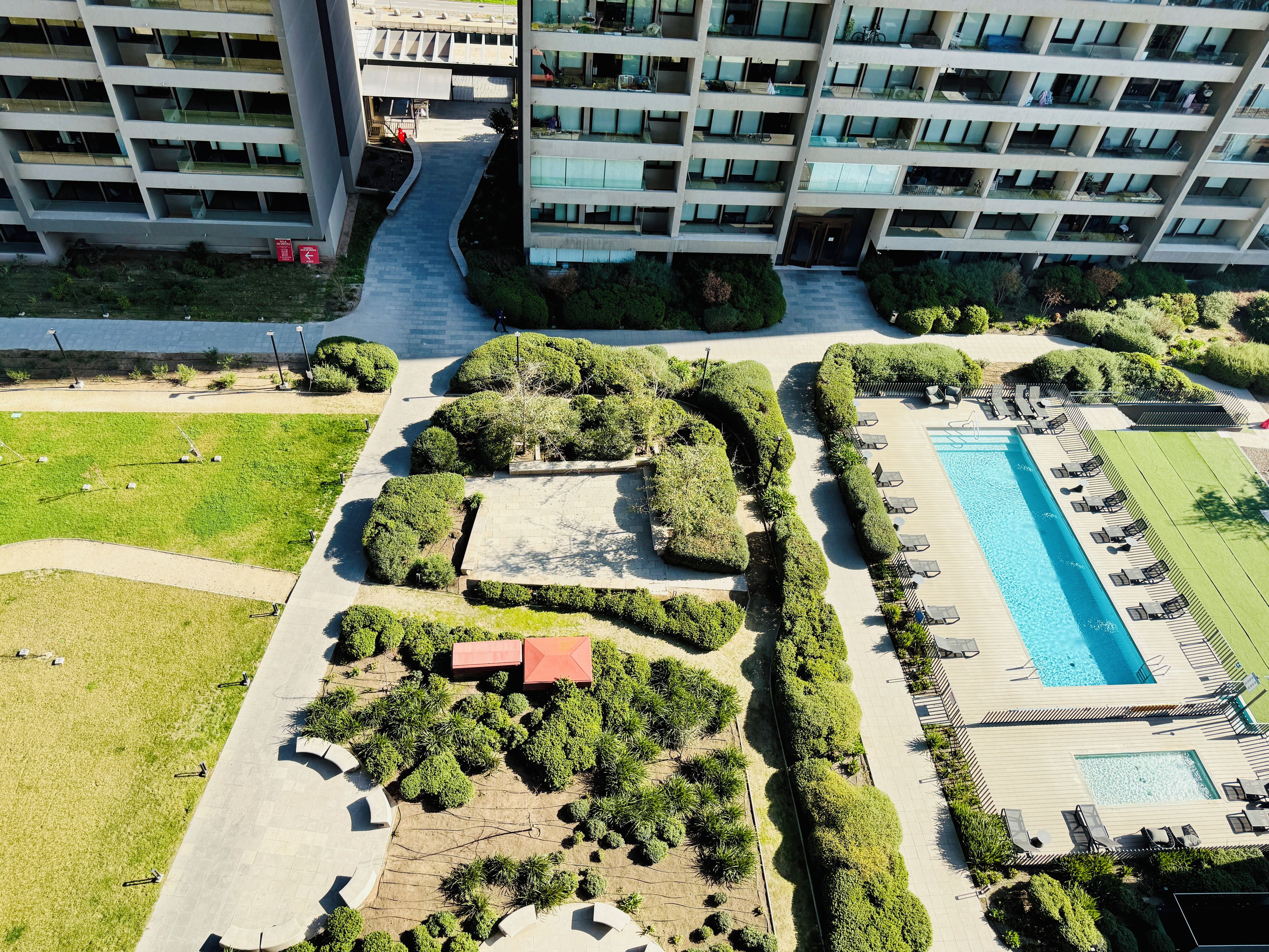 Vista aérea de un edificio moderno con varios balcones, un camino central y una zona de piscina con tumbonas.