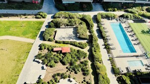 Vista aérea de um edifício moderno com várias varandas, um caminho central e uma área de piscina com espreguiçadeiras.