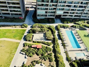 Vue aérienne d’un bâtiment moderne doté de nombreux balcons, d’un chemin central et d’un espace piscine avec des chaises longues.