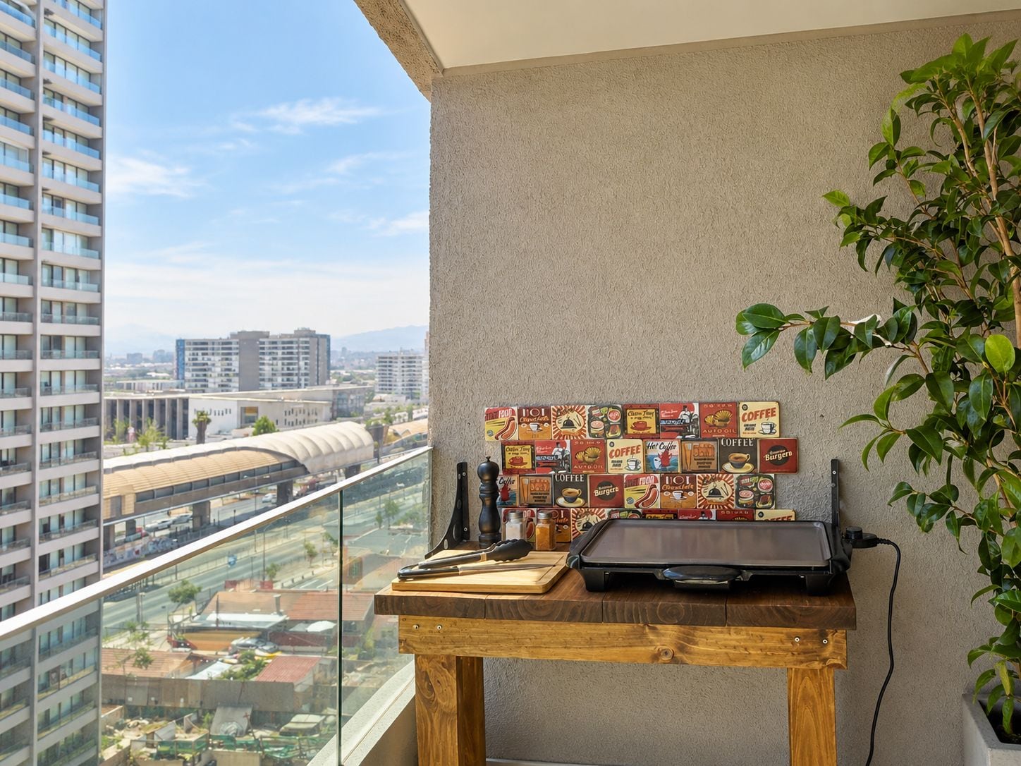 A balcony with a city view, a wooden table with a laptop, and a wall decorated with vintage coffee signs.