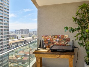 A balcony with a city view, a wooden table with a laptop, and a wall decorated with vintage coffee signs. - Aire Acond. | Estacionamiento | El mejor lugar (Santiago)