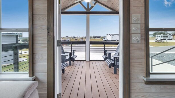 A wooden deck with outdoor seating, a ceiling fan, and large windows offering a view of the surrounding area. - Luxury Das Blumenhaus (Fredericksburg)