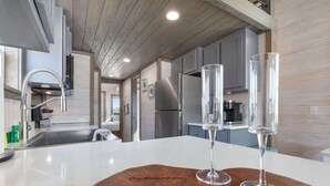 A modern kitchen with a central island, stainless steel appliances, and a wooden backsplash. - Luxury Das Blumenhaus (Fredericksburg)