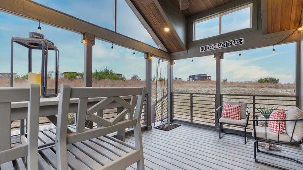 A covered outdoor deck with seating, a view of the beach, and a sign indicating the location as LUCKENBACH TEXAS. - There’s No Lookin’ Bach (Fredericksburg)