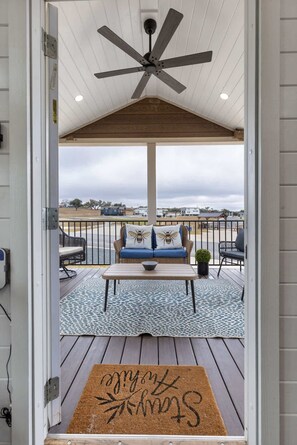A covered outdoor seating area with a ceiling fan, a bench with cushions, and a view of the surrounding landscape. - Vine and Dandee - Prime Location | Pet Friendly (Fredericksburg)