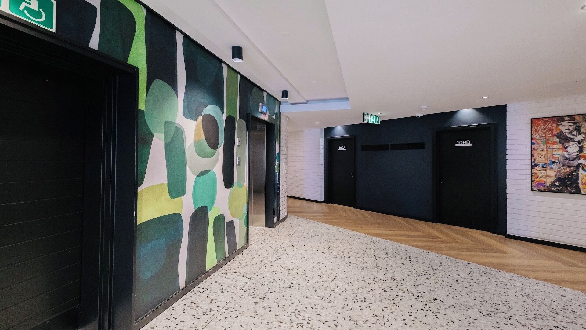 Un couloir avec un sol à motifs, un panneau vert indiquant qu’il est accessible aux personnes en fauteuil roulant, et une porte portant le numéro « 109A ».