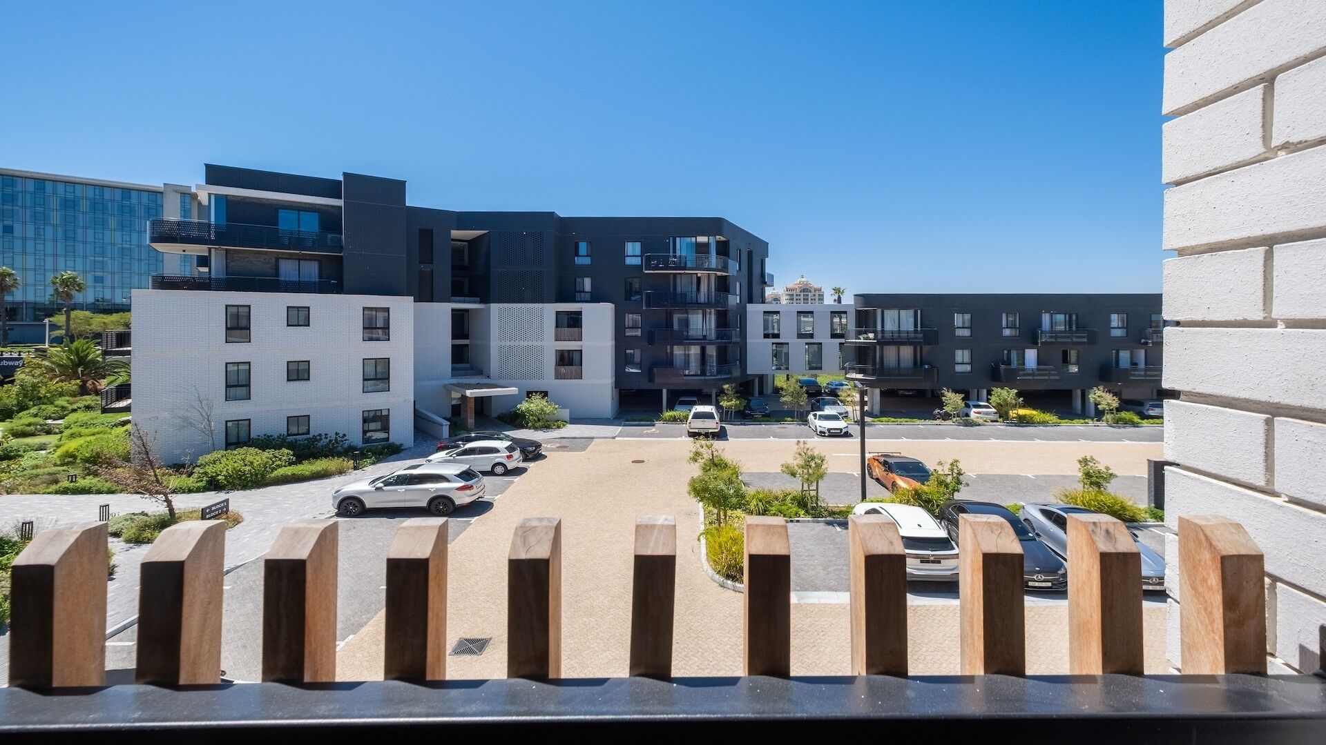 Un bâtiment moderne à plusieurs étages, un parking avec plusieurs voitures et un ciel dégagé.