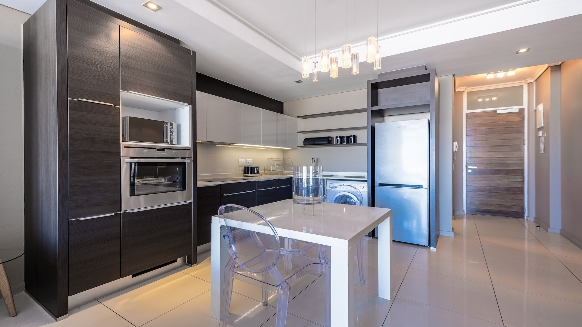 A modern kitchen with dark cabinetry, stainless steel appliances, and a glass-top table.