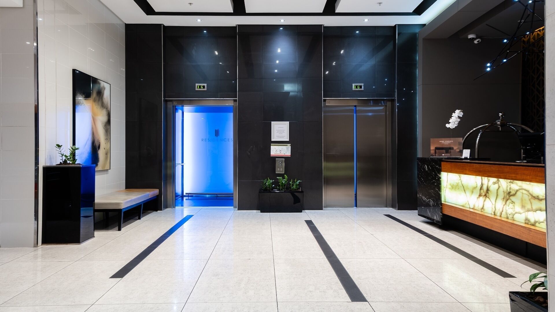 A modern lobby with a reception desk, a bench, and two elevators.