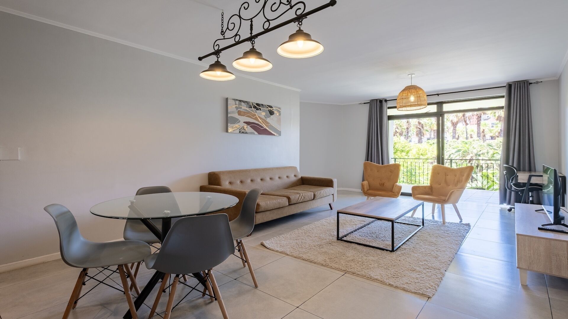 Un salon moderne comprenant un canapé, des fauteuils, une table basse et une table à manger. Il y a un balcon avec vue sur la verdure.