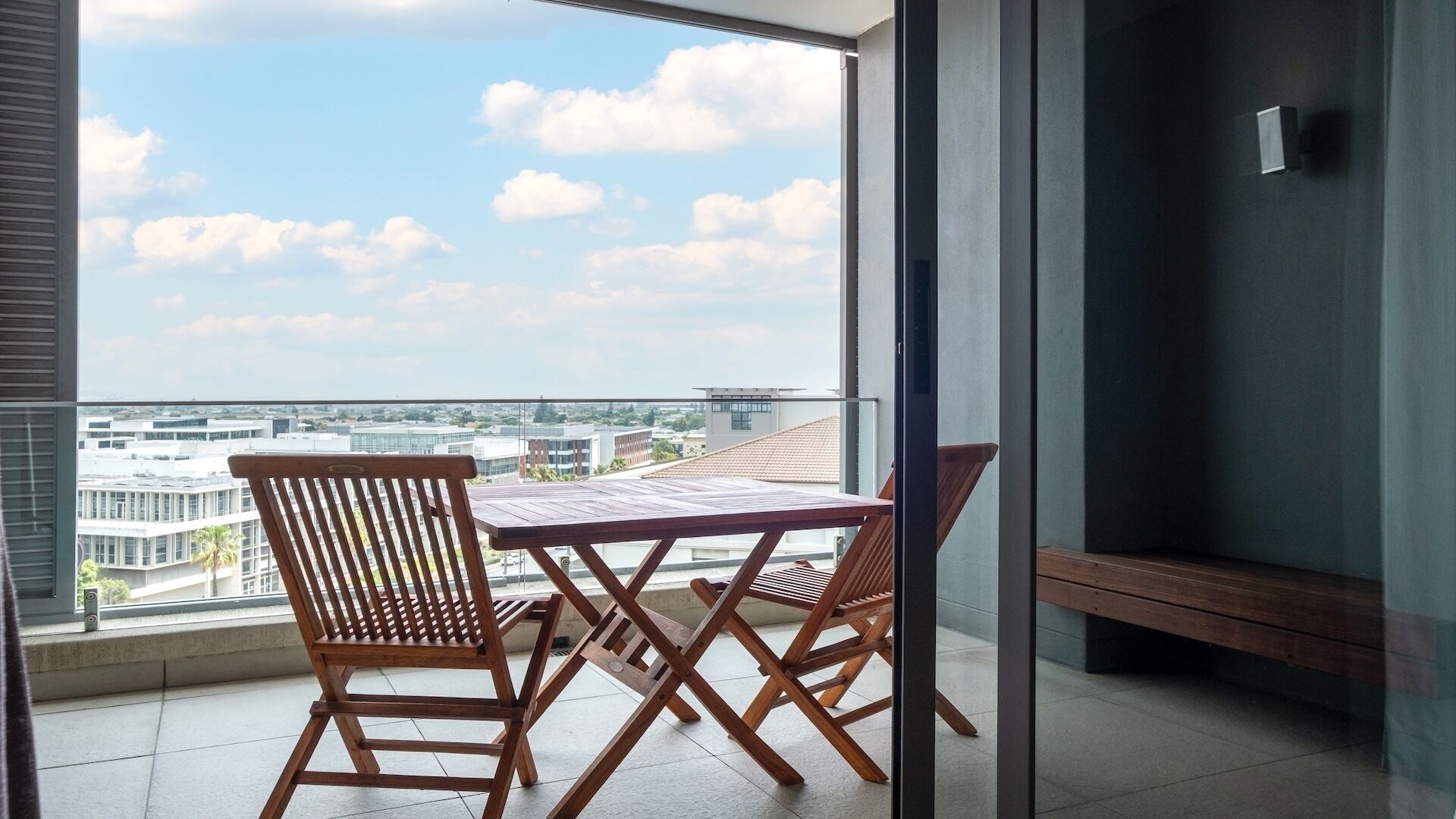 Een balkon met uitzicht op de stad, twee houten stoelen en een kleine tafel.