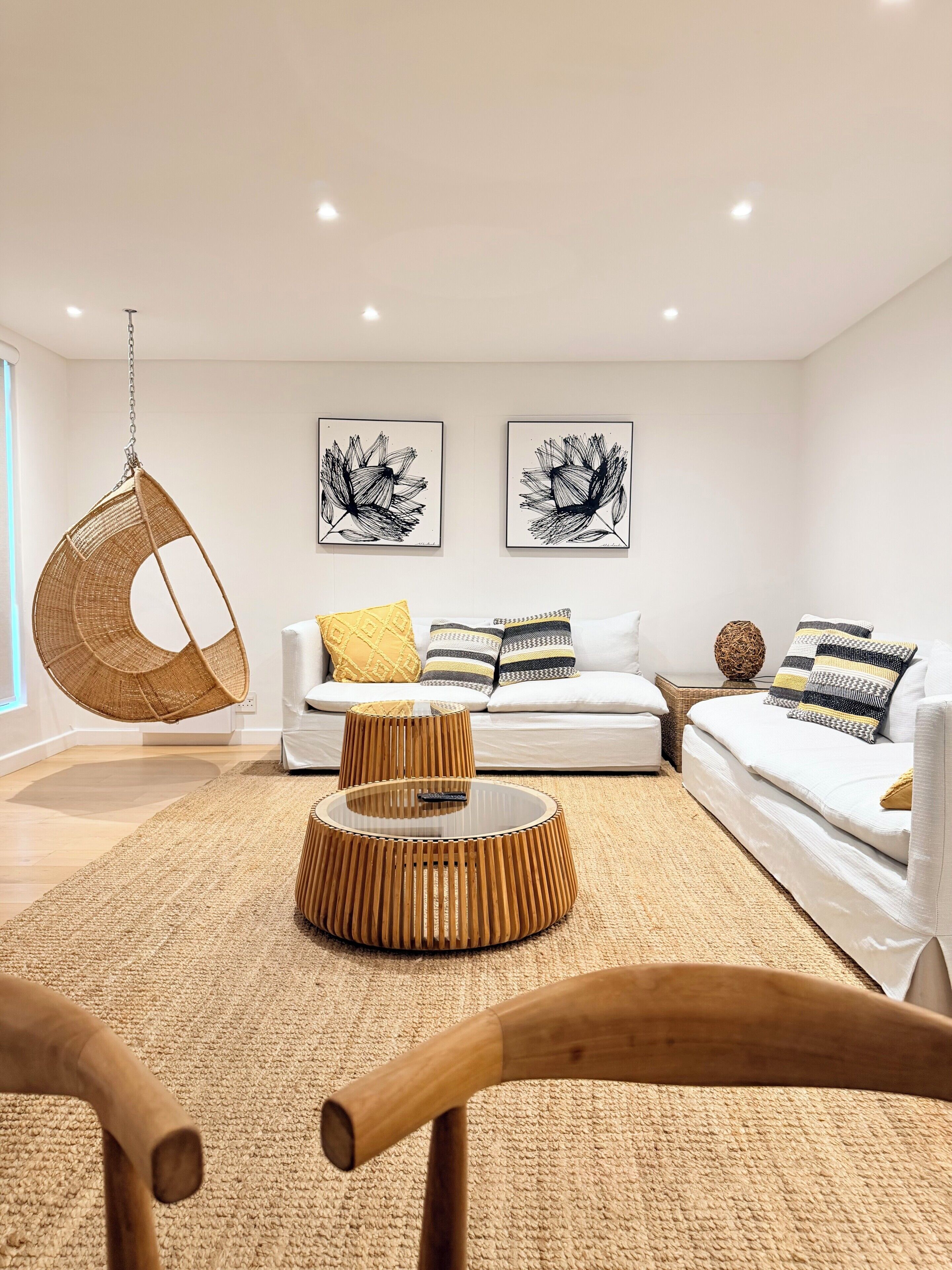 A modern living room with a hanging chair, a round coffee table, a sofa, and two wall art pieces.