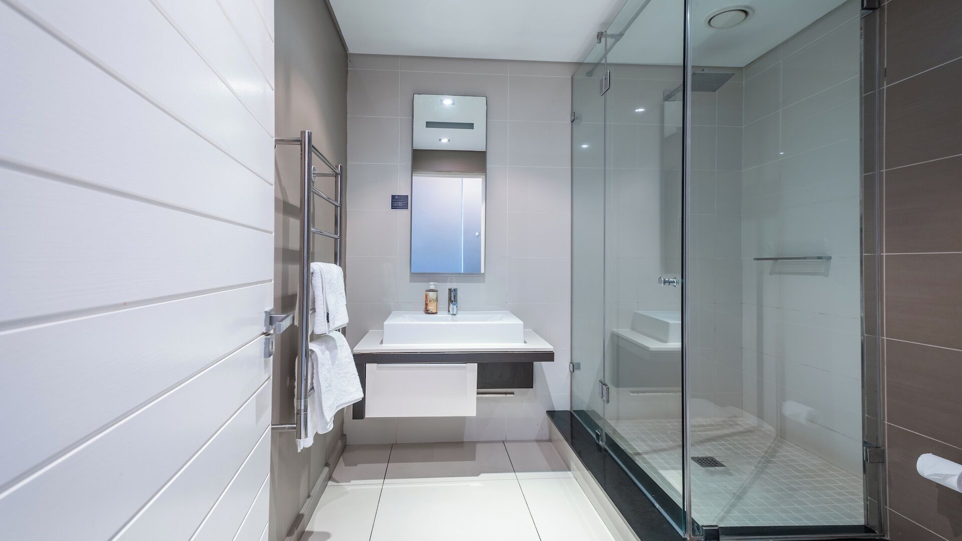 Un baño moderno con ducha de vidrio, lavabo blanco y espejo sobre él.