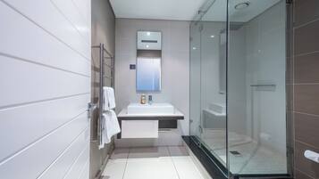Un baño moderno con ducha de vidrio, lavabo blanco y espejo sobre él.