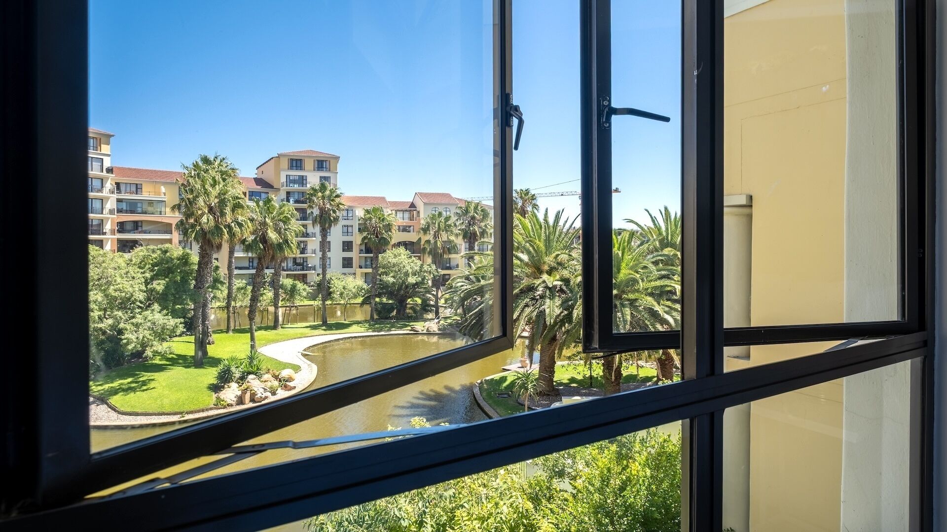 Une vue d’un hôtel avec une piscine, des palmiers et, au loin, des immeubles à plusieurs étages.