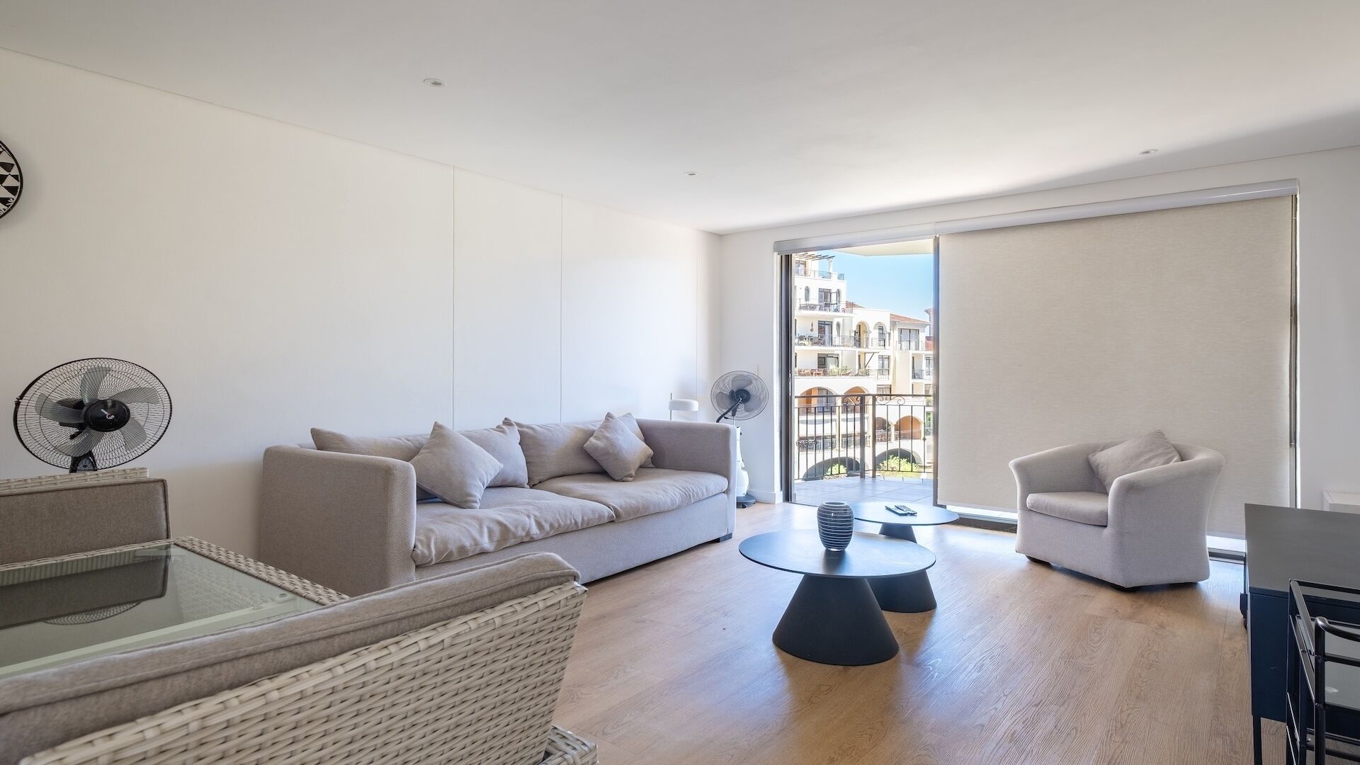 Un salon moderne comprenant un canapé, deux fauteuils, une table basse et un ventilateur.