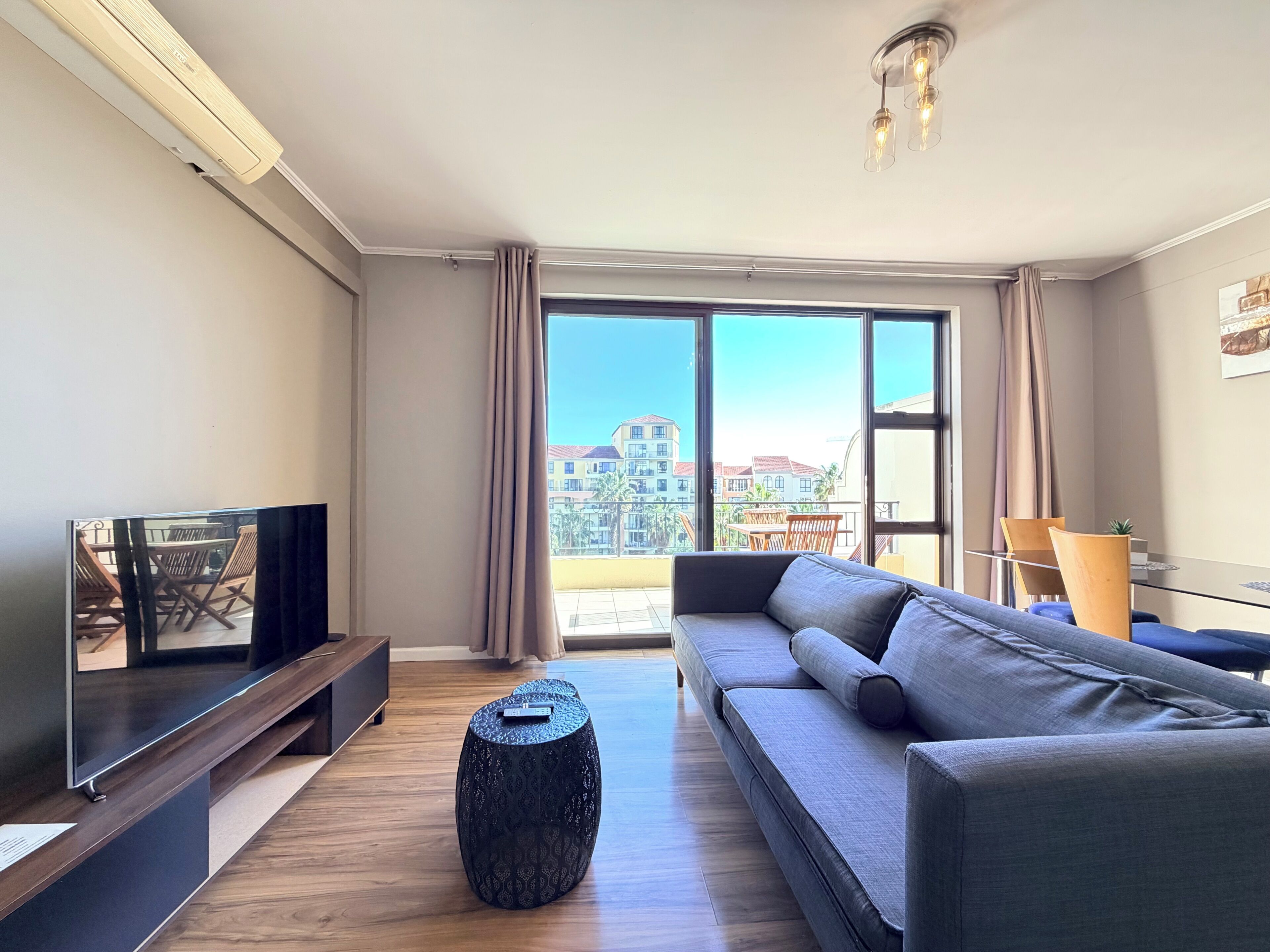 A modern living room with a sofa, TV, and a balcony with a view of buildings.