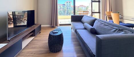 A modern living room with a sofa, TV, and a balcony with a view of buildings.