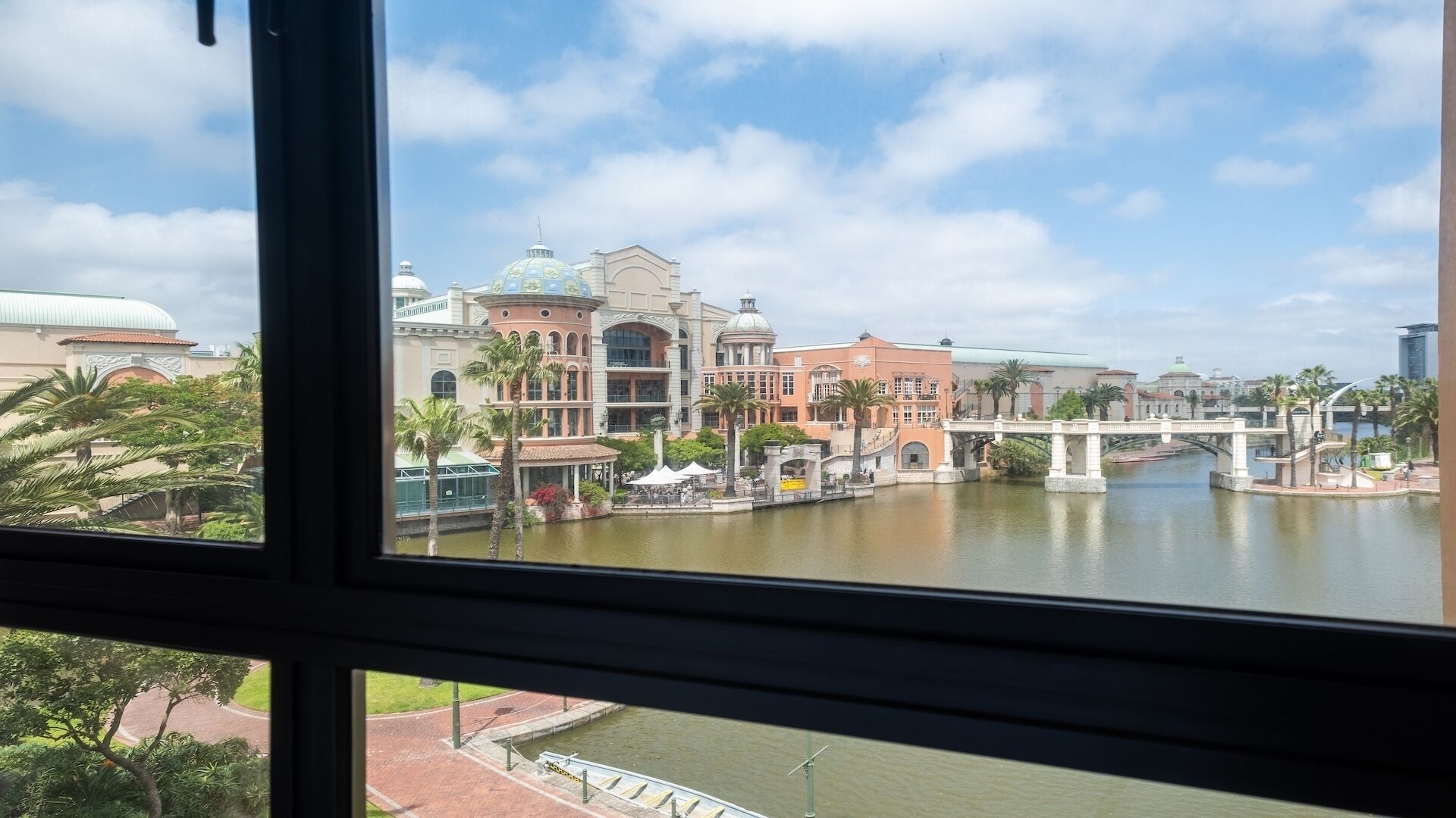 A view of a riverside area with buildings, palm trees, and a bridge.
