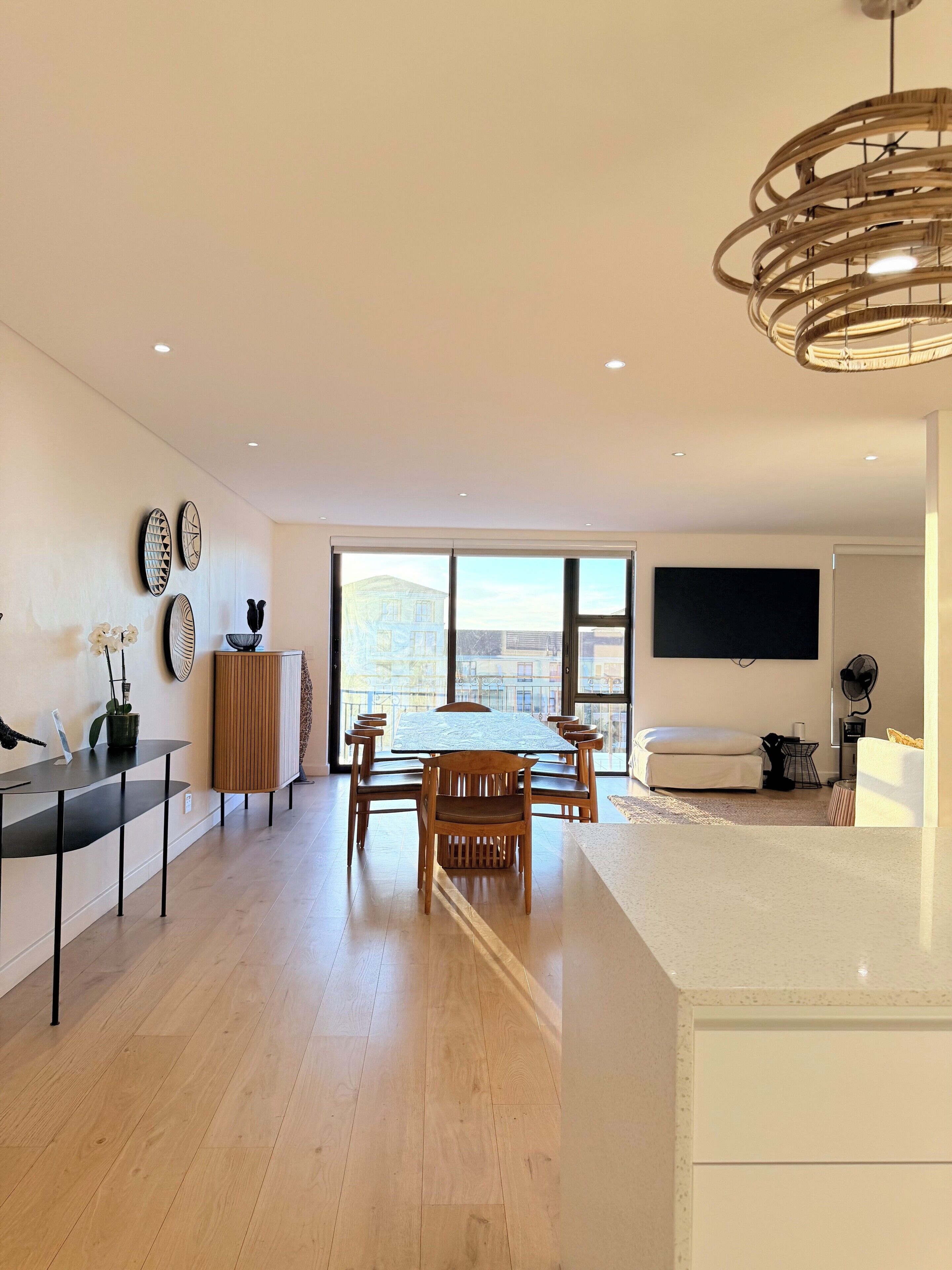 Un salon moderne comprenant un coin repas, un parquet en bois et une grande fenêtre donnant sur la ville.