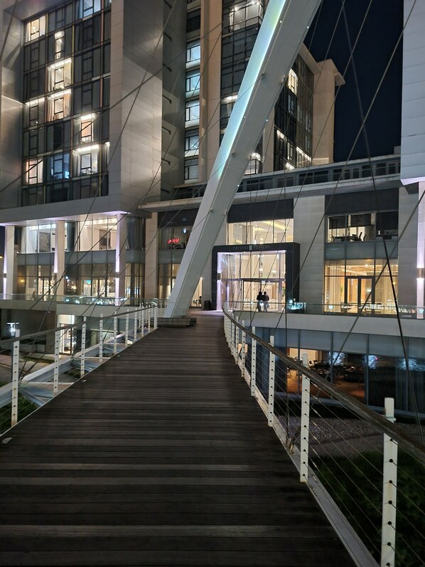 Un bâtiment moderne doté d’une passerelle en bois et de rampes de protection en verre, comprenant plusieurs étages et un escalier imposant.