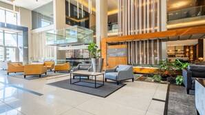 A spacious lobby with a high ceiling, modern furniture, a glass staircase, and a bar area.