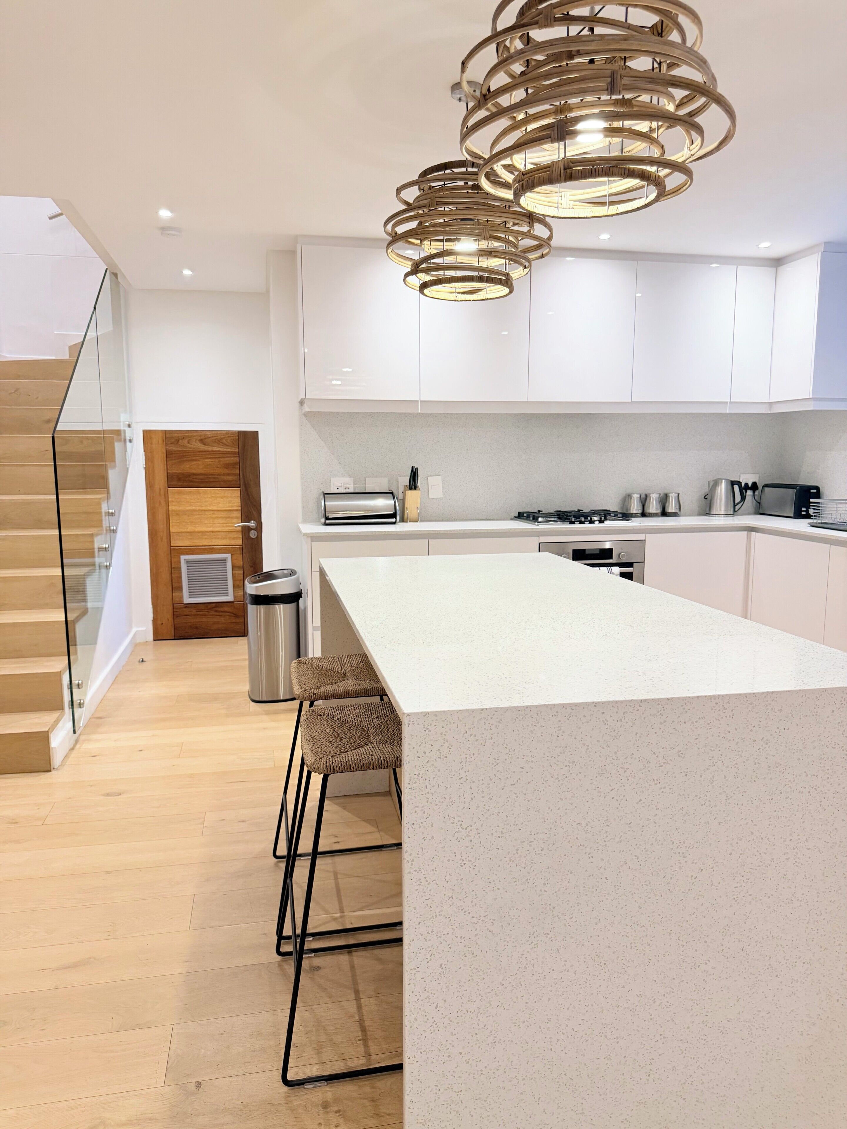 A modern kitchen with a central island, white cabinetry, and a unique circular chandelier.