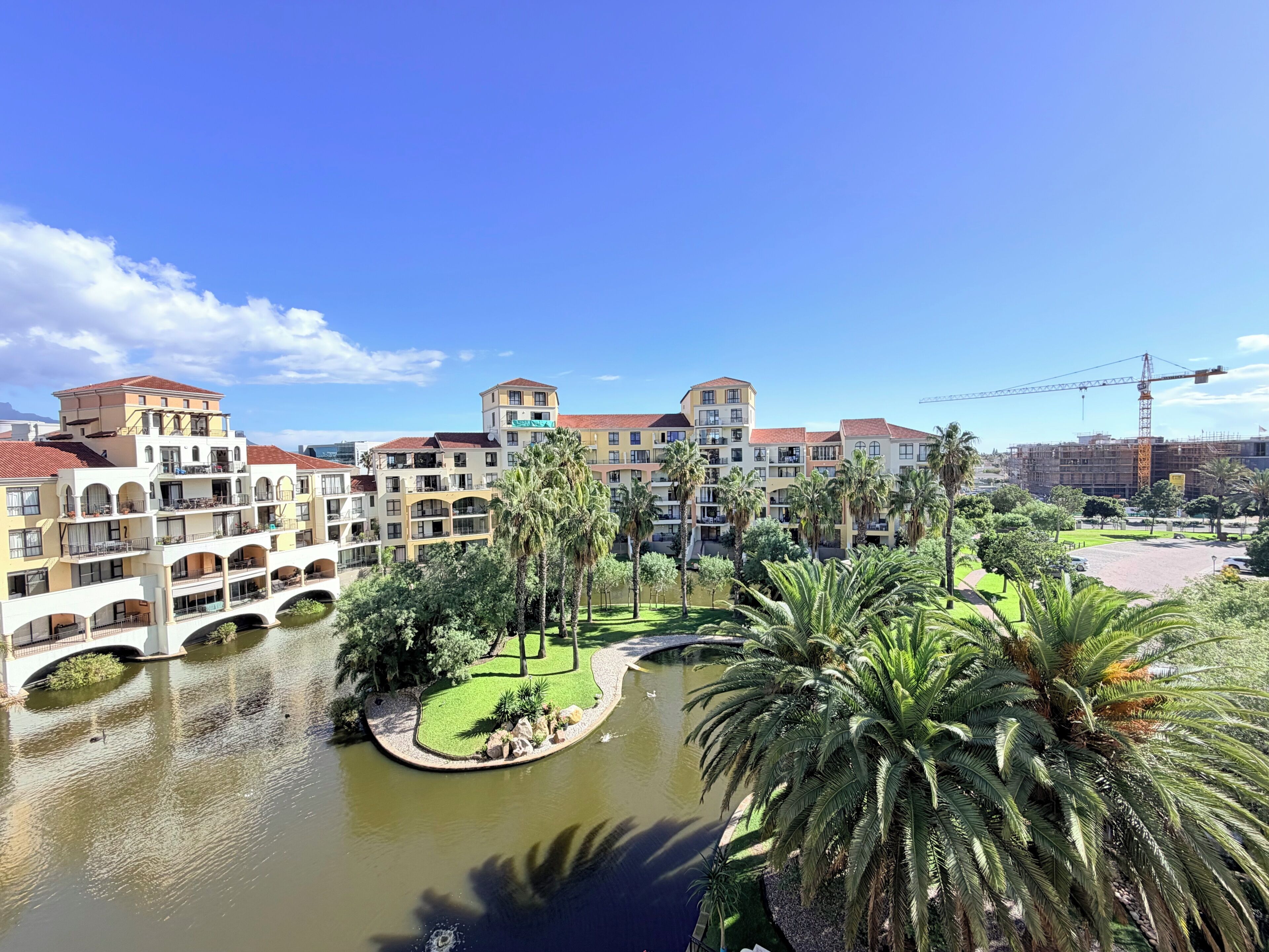 A multi-story hotel with balconies, a courtyard with palm trees, and a river.