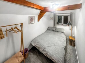 Ein Schlafzimmer mit einem Bett, Holzbalken, einem Fenster, einem Kleiderständer und einem kleinen Korb.