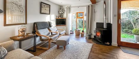 A cozy living room with a fireplace, comfortable seating, and a view of the garden.
