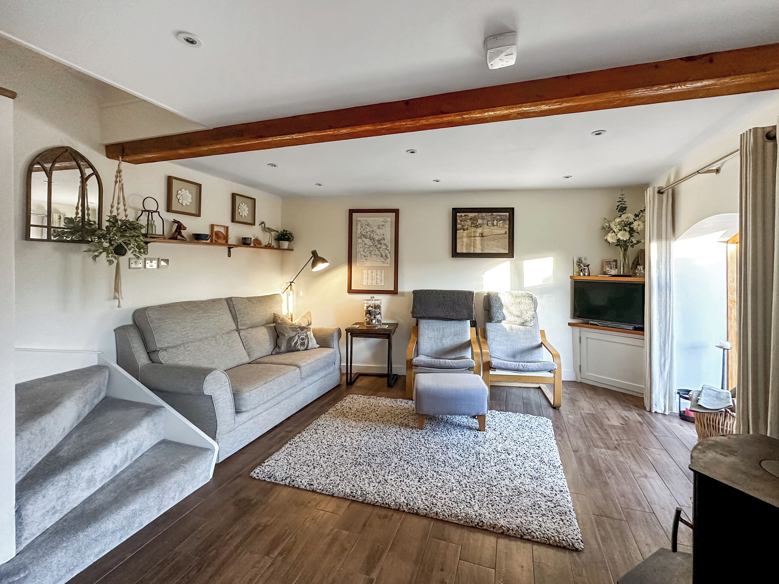 Un salon avec un canapé gris, deux fauteuils, un plancher en bois, un plafond blanc et une cheminée.