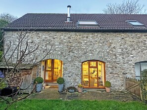 A stone house with two large arched windows, a chimney, and a small garden area with potted plants. - 2 bedroom accommodation in Combe Raleigh (Combe Raleigh)