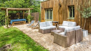 Un área de estar al aire libre con mobiliario de mimbre, una pérgola de madera y un muro de piedra.