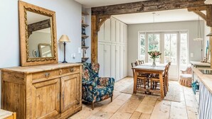 Un comedor rústico con una mesa y sillas de madera, un sillón floral y un espejo sobre un aparador de madera.