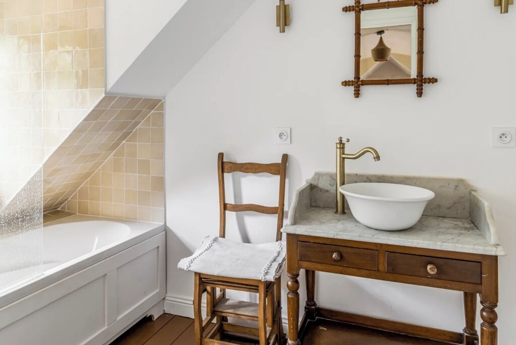 A bathroom with a bathtub, a wooden chair, a marble sink, and a mirror.