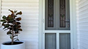 A house entrance with a white door, a potted plant, and a welcome mat. - The Farmhouse Dunedoo (Dunedoo)