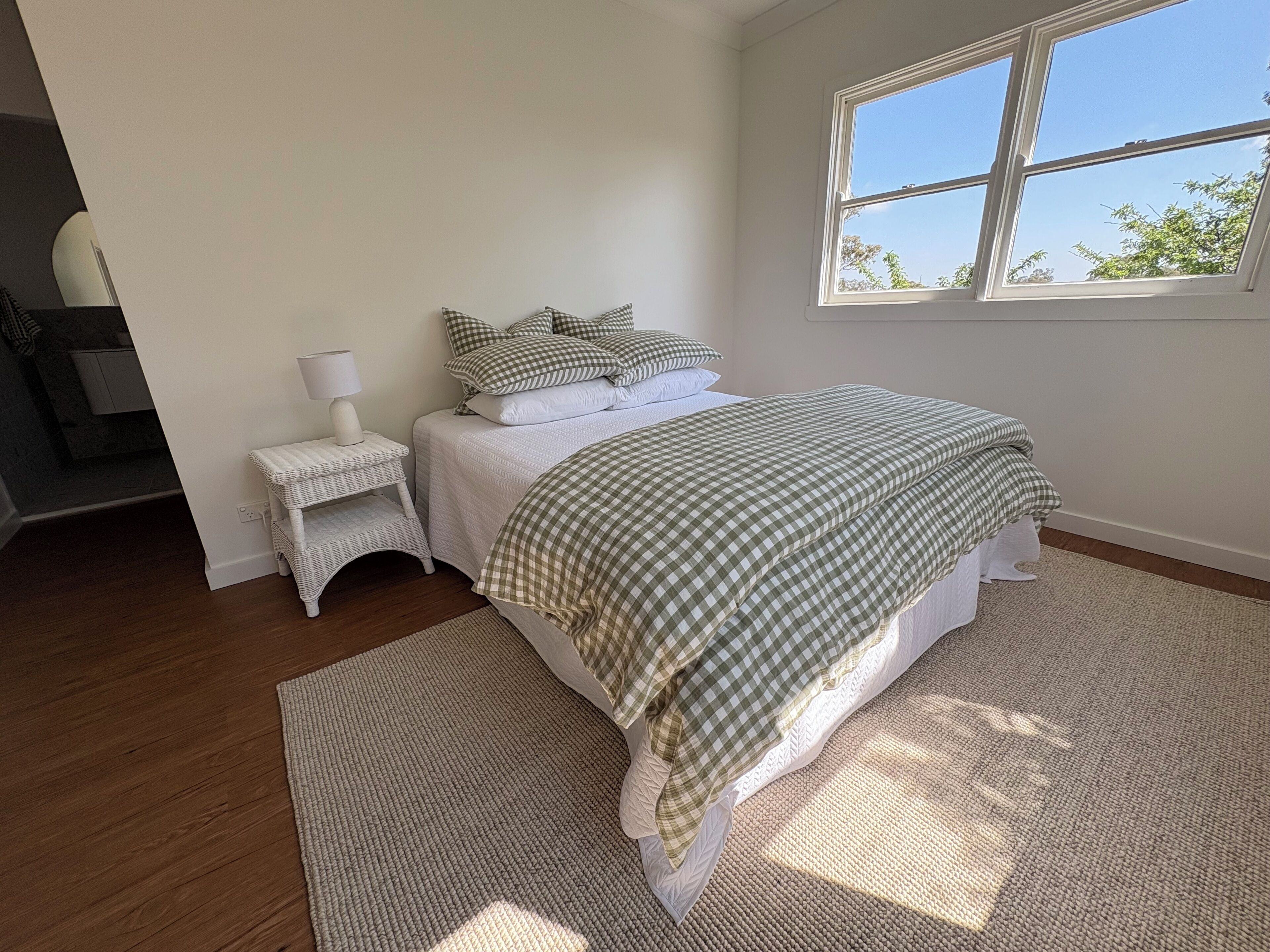 A bedroom with a bed, a nightstand, a window, and a view of the outdoors.